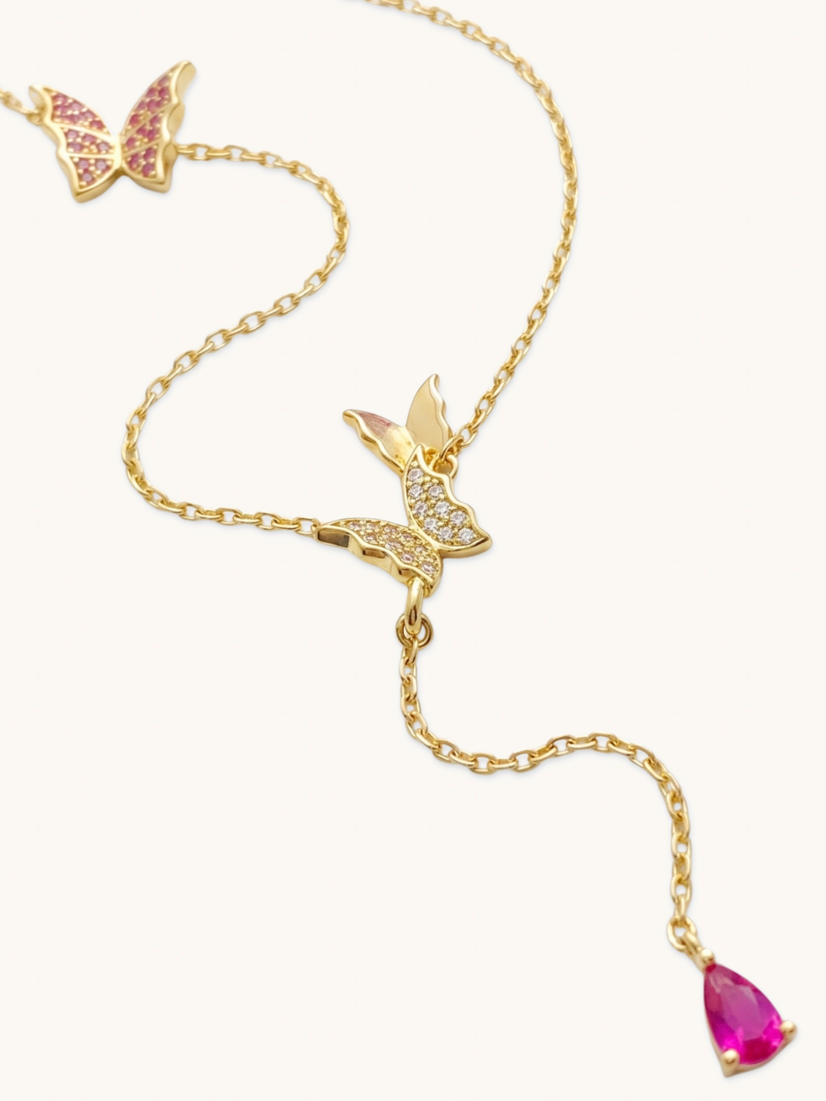 Close up of the Astrid necklace butterfly charms and pink pear cut cubic zirconia drop in gold plated sterling silver