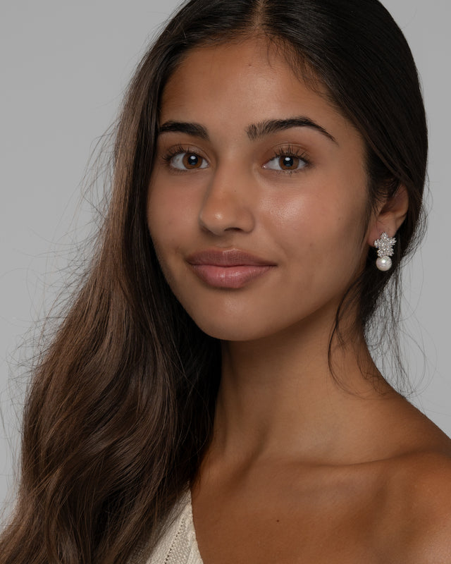 Model wearing the Blanca pearl flower stud earrings, front view against a soft grey backdrop